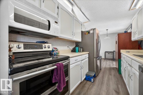 Galley kitchen featuring white cabinetry, light countertops, subway tile backsplash, stainless steel appliances, and wood-finish flooring - 5215 50 Avenue, Bruderheim, AB - Indoor Photo Showing Kitchen