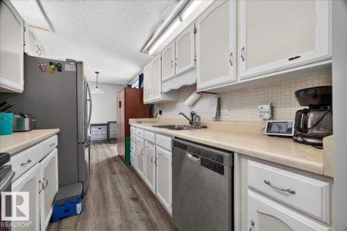 Kitchen featuring white cabinetry, light-toned countertops, a stainless steel dishwasher, a stainless steel refrigerator, and wood-finish flooring - 5215 50 Avenue, Bruderheim, AB - Indoor Photo Showing Kitchen