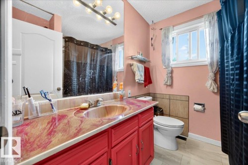 Bathroom featuring a bright window, light tile flooring, and a vanity with red cabinetry and an integrated basin sink - 5215 50 Avenue, Bruderheim, AB - Indoor Photo Showing Bathroom