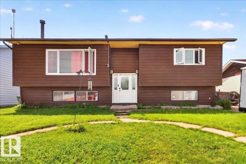 Brown horizontal siding exterior with a white entry door, white window frames, and a green grass lawn with concrete stepping stones - 5215 50 Avenue, Bruderheim, AB - Outdoor With Exterior