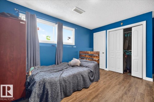 Interior room featuring wood-finish flooring, two rectangular windows, a white ceiling, and blue painted walls - 5215 50 Avenue, Bruderheim, AB - Indoor Photo Showing Bedroom
