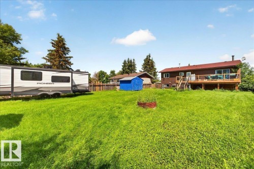 Expansive green yard with a wooden privacy fence and a blue storage shed - 5215 50 Avenue, Bruderheim, AB - Outdoor With Deck Patio Veranda