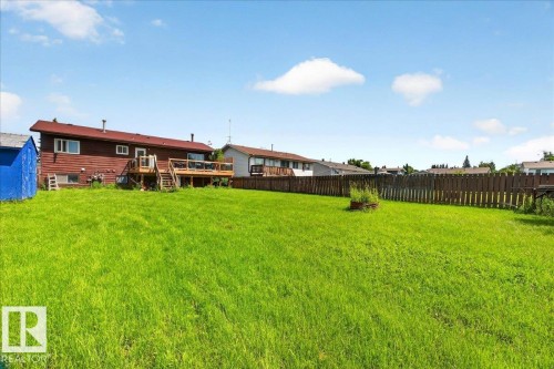 Expansive green yard featuring a multi-level wood deck with stairs, a privacy fence, and wood siding on the home - 5215 50 Avenue, Bruderheim, AB - Outdoor