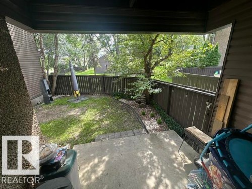 Covered patio with concrete flooring, framed by a dark brown horizontal fence, and featuring a small lawn area with surrounding landscaping - 18020 96 Avenue, Edmonton, AB 