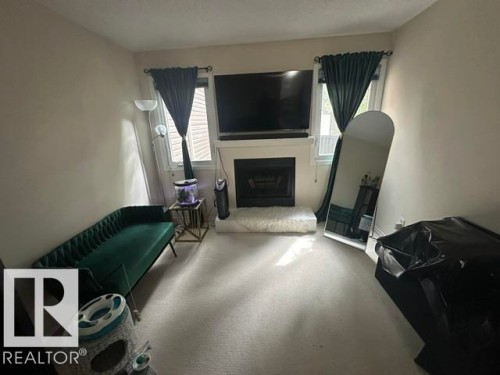 Living area featuring a central fireplace with a white mantel, two windows with louvered blinds, and light-colored wall-to-wall carpeting - 18020 96 Avenue, Edmonton, AB 
