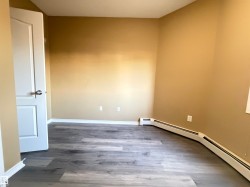 Interior space featuring wood-finish flooring, light tan walls, baseboard heating, and a white two-panel interior door - 