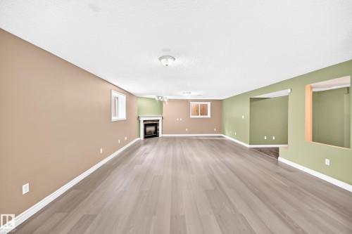 Spacious room featuring wood-finish flooring, a fireplace with a white mantel, and neutral wall tones - 13124 36 Street, Edmonton, AB 