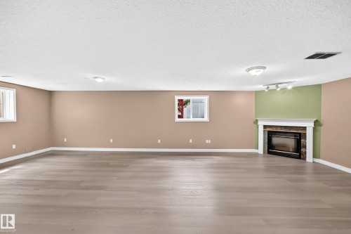 Spacious room featuring wood-finish flooring, a built-in corner fireplace with stone surround and white mantel, and multiple windows - 13124 36 Street, Edmonton, AB 