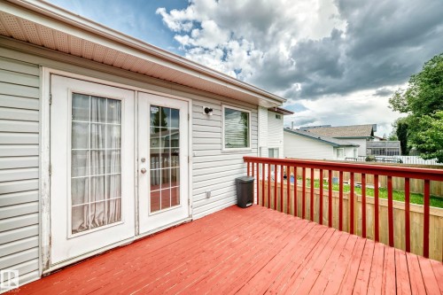 Rear exterior deck featuring red-stained wood flooring and railing, white vinyl siding, and white French patio doors - 13124 36 Street, Edmonton, AB 