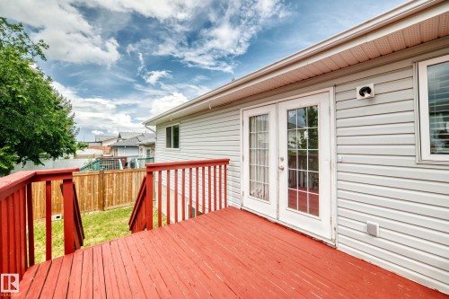 Exterior deck featuring red-stained wood planking and matching railings, offering direct access to the interior through white French doors with divided lites - 13124 36 Street, Edmonton, AB 
