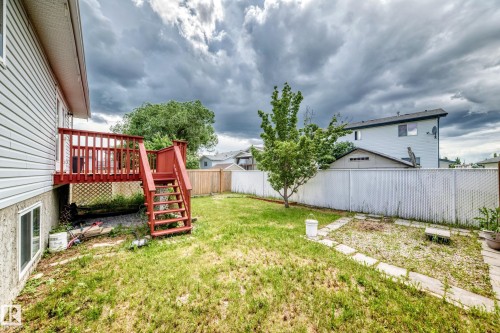 Spacious backyard featuring a red-stained wooden deck with stairs, a privacy fence, established trees, and stone paver accents - 13124 36 Street, Edmonton, AB 