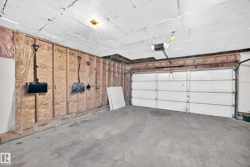 Attached garage featuring a concrete floor, exposed wood framing, and a white paneled garage door with an automatic opener - 13124 36 Street, Edmonton, AB 
