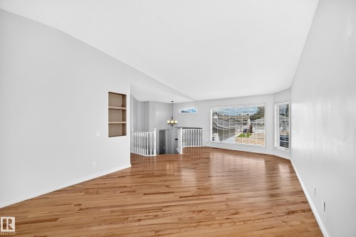Bright interior featuring wood-finish flooring, a contemporary chandelier, a built-in shelving niche, and large windows - 13124 36 Street, Edmonton, AB 