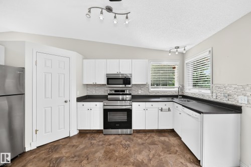 Kitchen featuring white cabinetry, dark countertops, stainless steel appliances, a mosaic tile backsplash, and wood-finish flooring - 13124 36 Street, Edmonton, AB 