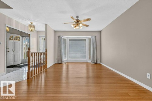 Open-concept living area featuring wood-finish flooring, a bay window with drapes, and a ceiling fan with integrated lighting - 16524 99 Street, Edmonton, AB 