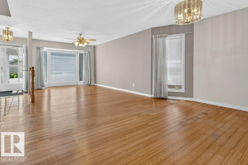 Spacious interior featuring wood-finish flooring, neutral wall paint, and a bay window with blinds - 16524 99 Street, Edmonton, AB 