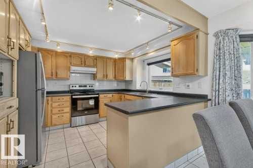 U-shaped kitchen featuring wood cabinetry, dark countertops, white tile backsplash, and tile flooring - 16524 99 Street, Edmonton, AB 