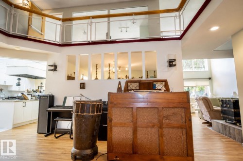 Open-concept interior featuring wood-finish flooring, a kitchen area with white cabinetry and light-toned countertops, and a balcony with a glass and wood railing overlooking the main living space - 60528 Range Road 112, Rural St. Paul County, AB 