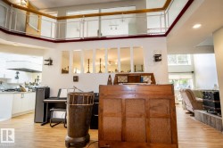 Open-concept interior featuring wood-finish flooring, a kitchen area with white cabinetry and light-toned countertops, and a balcony with a glass and wood railing overlooking the main living space - 