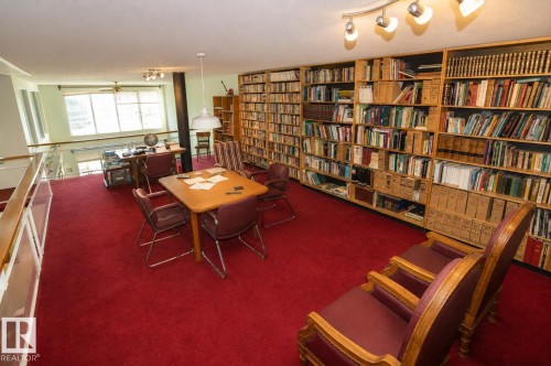 Loft space featuring extensive built-in wooden bookshelves, wall-to-wall red carpeting, and a track lighting fixture - 60528 Range Road 112, Rural St. Paul County, AB 