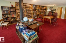 Expansive room featuring floor-to-ceiling built-in bookshelves, plush red carpeting, recessed lighting, and a white pendant light fixture - 