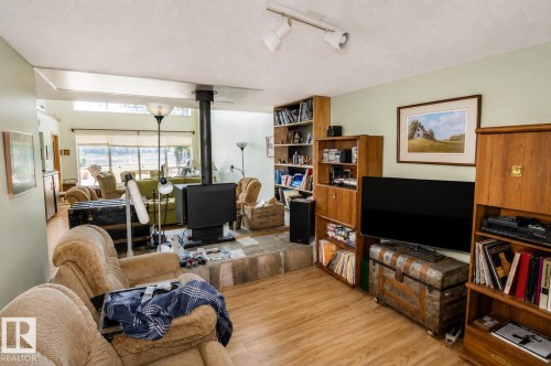 Spacious living area featuring wood-finish flooring and a stone hearth with a central wood-burning stove - 60528 Range Road 112, Rural St. Paul County, AB 
