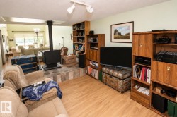 Open-concept living space featuring wood-finish flooring, a tiered floor design, a black wood-burning stove with a stone-look tile base, built-in wooden shelving, and track lighting - 