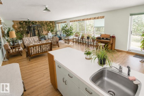 Spacious interior featuring wood-finish flooring, a kitchen island with an integrated stainless steel sink and faucet, ample natural light through multiple windows, and a sliding glass door leading to an exterior area - 60528 Range Road 112, Rural St. Paul County, AB 