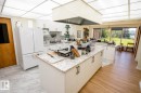Kitchen featuring a large central island with a light-toned countertop, white cabinetry, integrated appliances, and a full wall of windows - 60528 Range Road 112, Rural St. Paul County, AB 