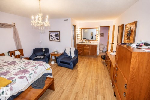 Spacious room featuring wood-finish flooring, a crystal chandelier, and a built-in vanity with a large mirror and task lighting - 60528 Range Road 112, Rural St. Paul County, AB 