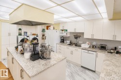 Spacious kitchen featuring an expansive center island with light granite countertops, extensive white cabinetry, a built-in dishwasher, and a double basin sink - 
