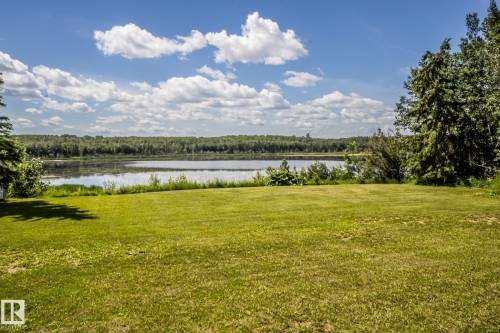 Expansive grassy area bordering a serene body of water, framed by mature trees and lush distant foliage - 60528 Range Road 112, Rural St. Paul County, AB 