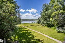 Expansive green lawn surrounded by mature trees, featuring a paved pathway - 