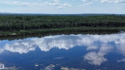 Expansive body of water reflecting a partly cloudy sky, bordered by a dense tree line - 
