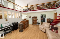 Open-concept living space featuring wood-finish flooring, a full-height ceiling, a second-story interior balcony with white railings, and a red carpeted spiral staircase - 