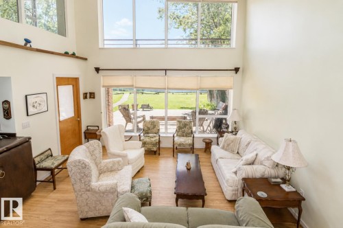 Two-story living area with wood-finish flooring, featuring a wall of windows, a high ceiling, and a light wood door - 60528 Range Road 112, Rural St. Paul County, AB 