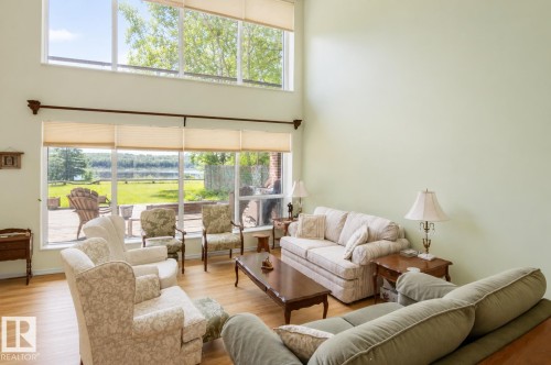 Living area featuring expansive windows, two-story ceiling, light green walls, wood-finish flooring, and a glass sliding door leading to an outdoor patio - 60528 Range Road 112, Rural St. Paul County, AB 