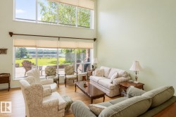 Living area featuring expansive windows, two-story ceiling, light green walls, wood-finish flooring, and a glass sliding door leading to an outdoor patio - 