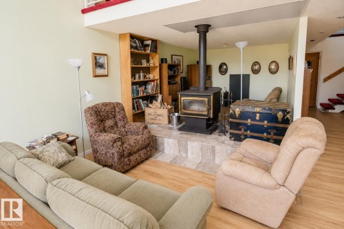 Living area featuring a freestanding wood stove on a tiled hearth, wood-finish flooring, and a built-in bookcase - 60528 Range Road 112, Rural St. Paul County, AB 