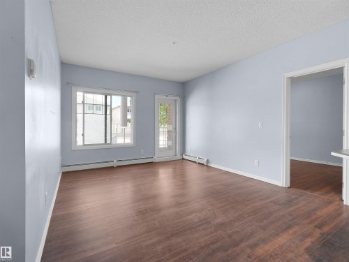 Spacious room featuring rich wood-finish flooring, light-toned wall paint, and a textured ceiling - 106 263 Macewan Road, Edmonton, AB 