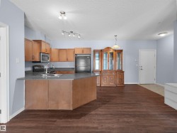 Open-concept kitchen featuring wood-finish cabinetry, stainless steel appliances, and a central island with a double basin sink - 