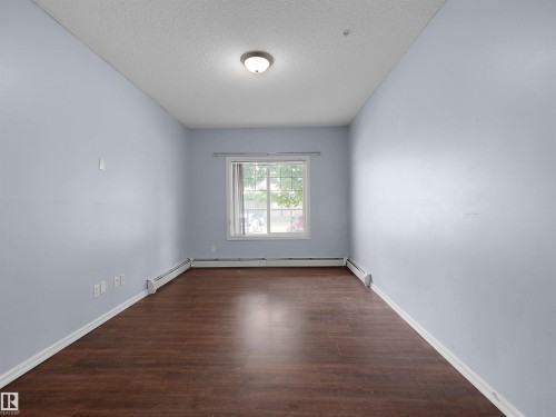 Spacious room featuring rich wood-finish flooring, light blue walls, and a white trim window - 106 263 Macewan Road, Edmonton, AB 