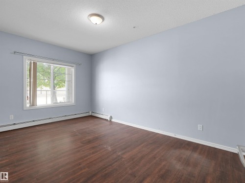 Spacious room featuring wood-finish flooring, light blue walls, and a large window - 106 263 Macewan Road, Edmonton, AB 