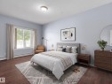 Spacious bedroom featuring wood-finish flooring, a large window with white trim, light blue wall paint, and a semi-flush ceiling light fixture - 106 263 Macewan Road, Edmonton, AB 