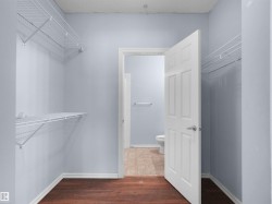 Walk-in closet featuring wood-finish flooring, white wire shelving, light blue walls, and a white paneled door with brushed nickel hardware - 