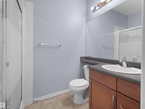 Full bathroom featuring a wood-finish vanity with an integrated sink, a large wall-mounted mirror, and a shower with a frosted glass enclosure - 106 263 Macewan Road, Edmonton, AB 
