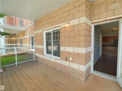 Private outdoor patio featuring wood-finish flooring, a light-colored soffit, and a glass and white railing system - 