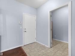 Entryway featuring a white door, light blue walls, and a contrasting floor with both wood-finish and patterned linoleum sections - 