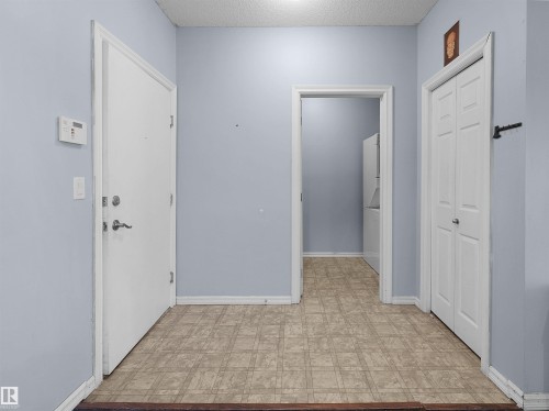 Entryway featuring light blue walls, patterned vinyl flooring, a white entry door with brushed nickel hardware, and a white bi-fold closet door - 106 263 Macewan Road, Edmonton, AB 
