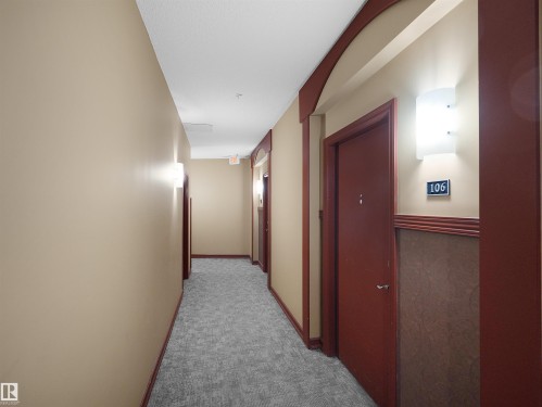 Hallway featuring textured carpeting, beige walls, and dark wood trim - 106 263 Macewan Road, Edmonton, AB 